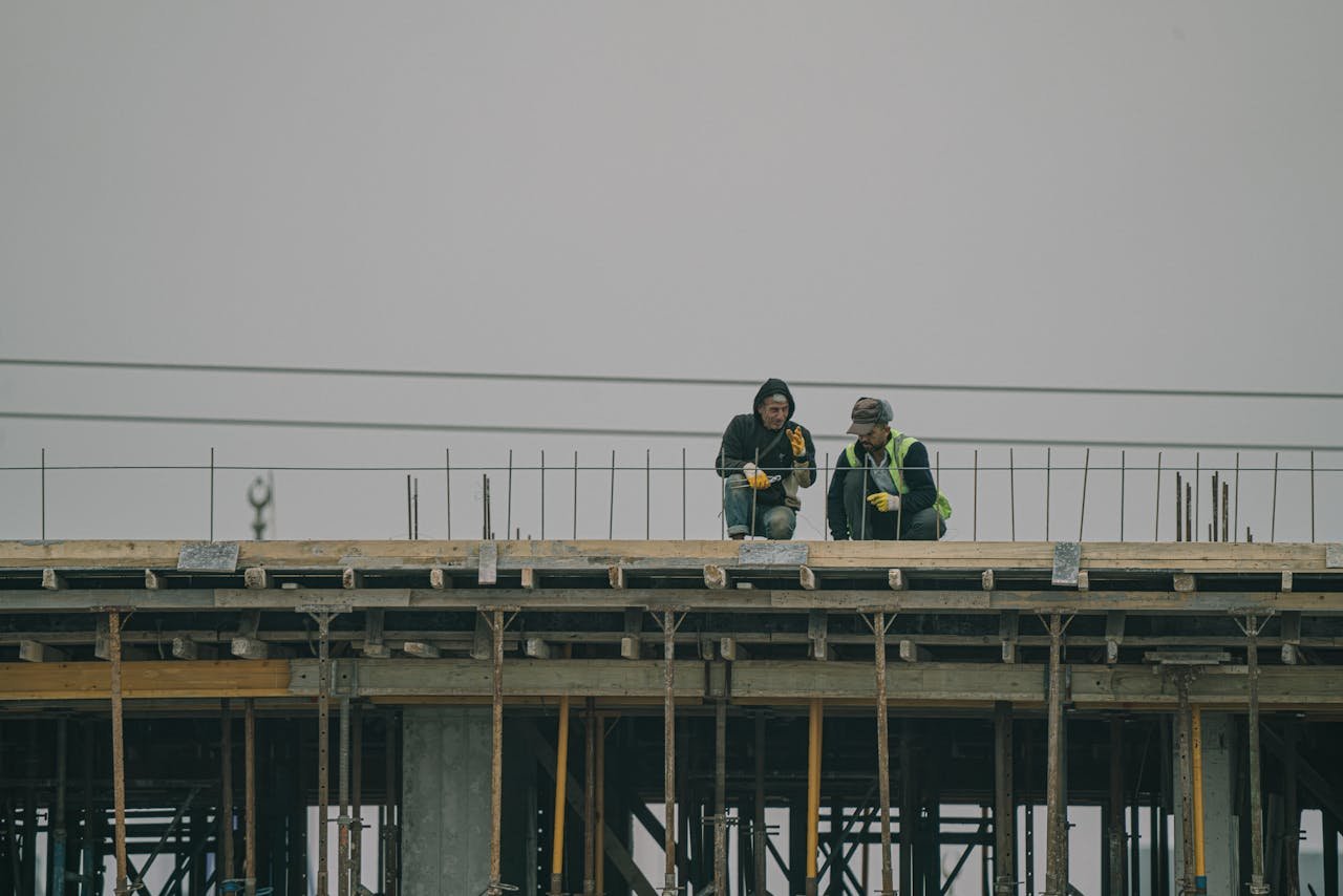Two construction workers on a building site in Denizli, Türkiye, working under overcast skies.